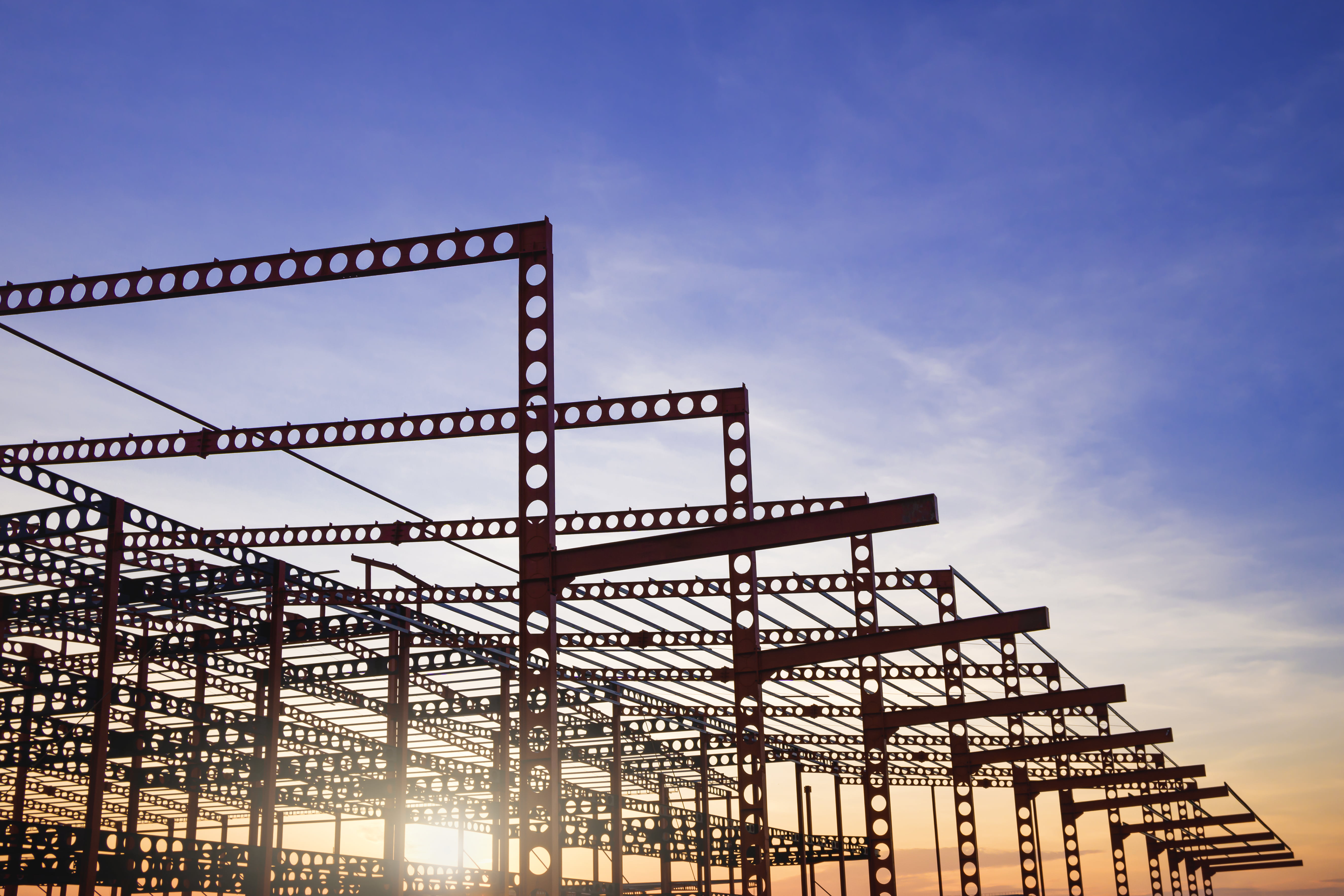 Silhouette of metal structure of large industrial building in construction site against sunset sky
